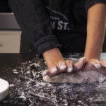 Black counter with flour and pizza dough being kneaded