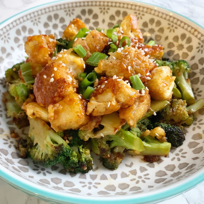 Tofu broccoli bowl with sesame seeds and green onions in a patterned bowl on a marble backdrop.