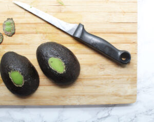 Two avocado hales faced-down with a small amount of the back flesh cut off so that they stand still in the oven.