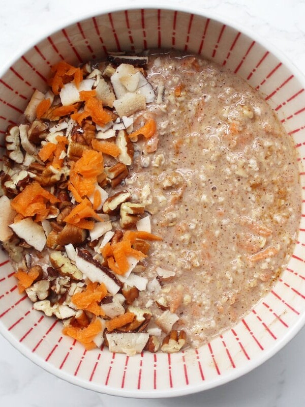 Carrot Cake Overnight Oats in a white and orange bowl. carrot, pecans and coconut on top.