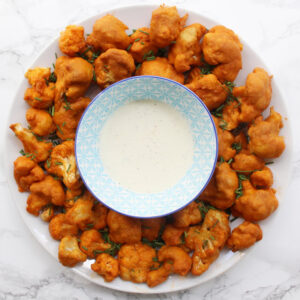 Spicy baked cauliflower wings on a round white plate with ranch dip in a blue patterned bowl in the middle