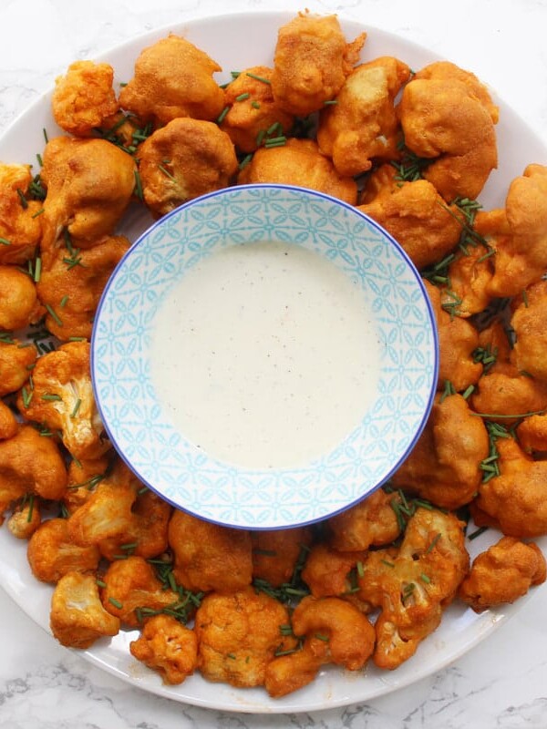 Spicy baked cauliflower wings on a round white plate with ranch dip in a blue patterned bowl in the middle