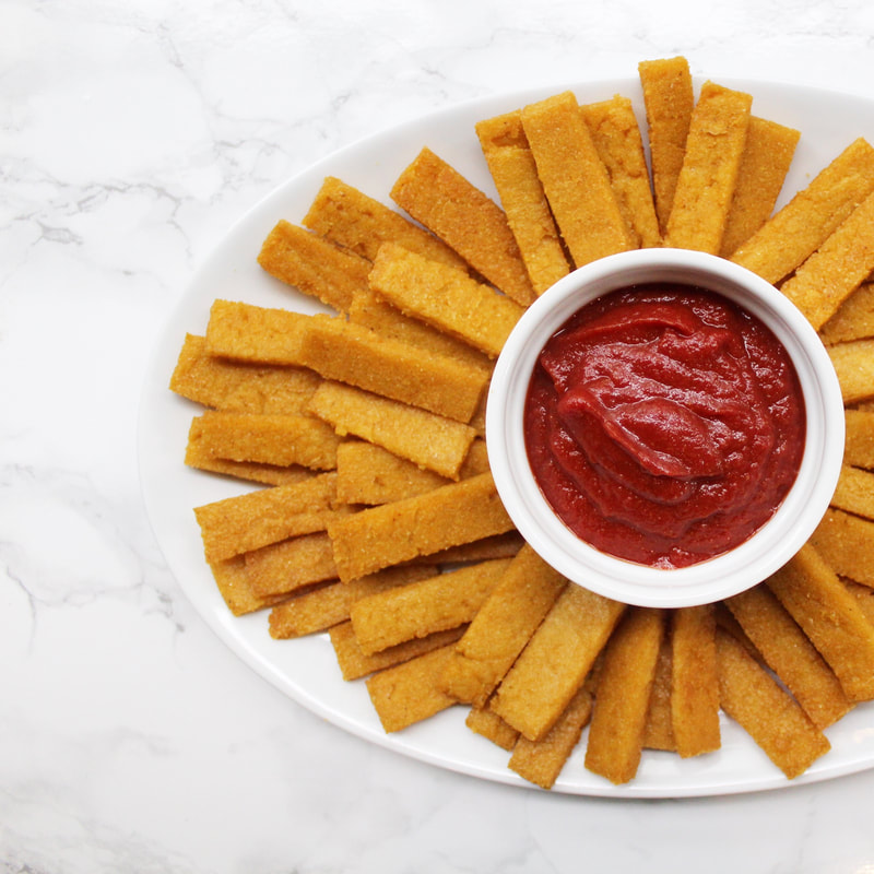 Baked polenta fries on a white plate with ketchup in the middle.