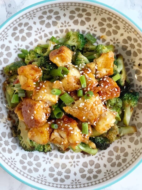 Tofu broccoli bowl with sesame seeds and green onions in a patterned bowl on a marble backdrop.