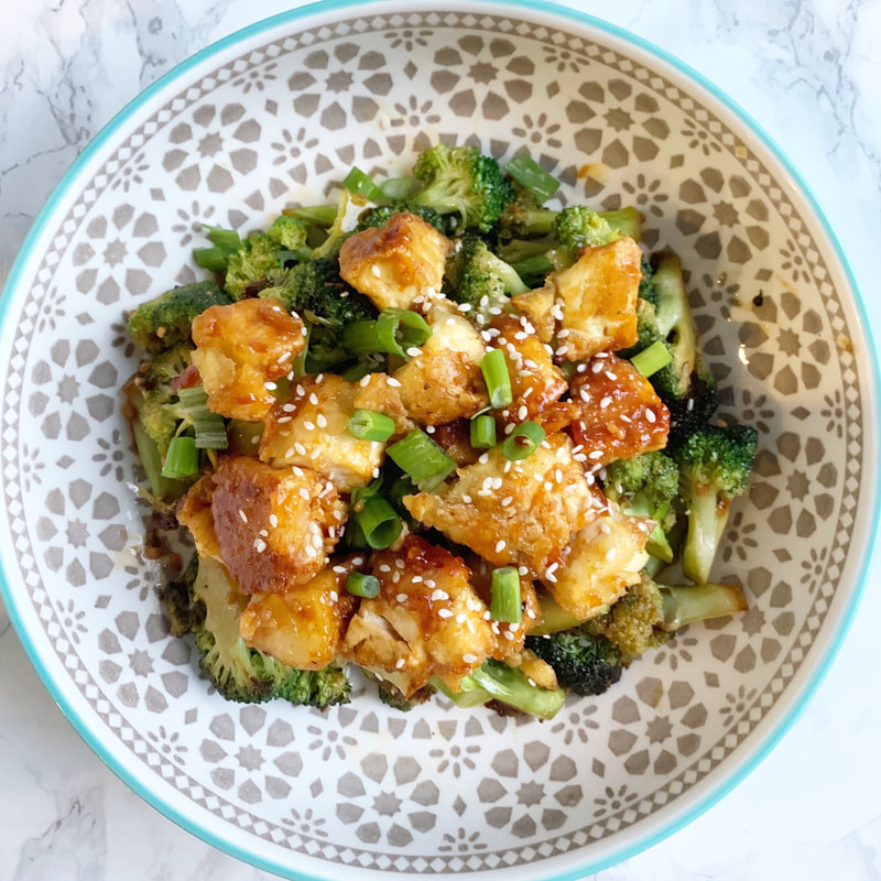 Tofu broccoli bowl with sesame seeds and green onions in a patterned bowl on a marble backdrop.