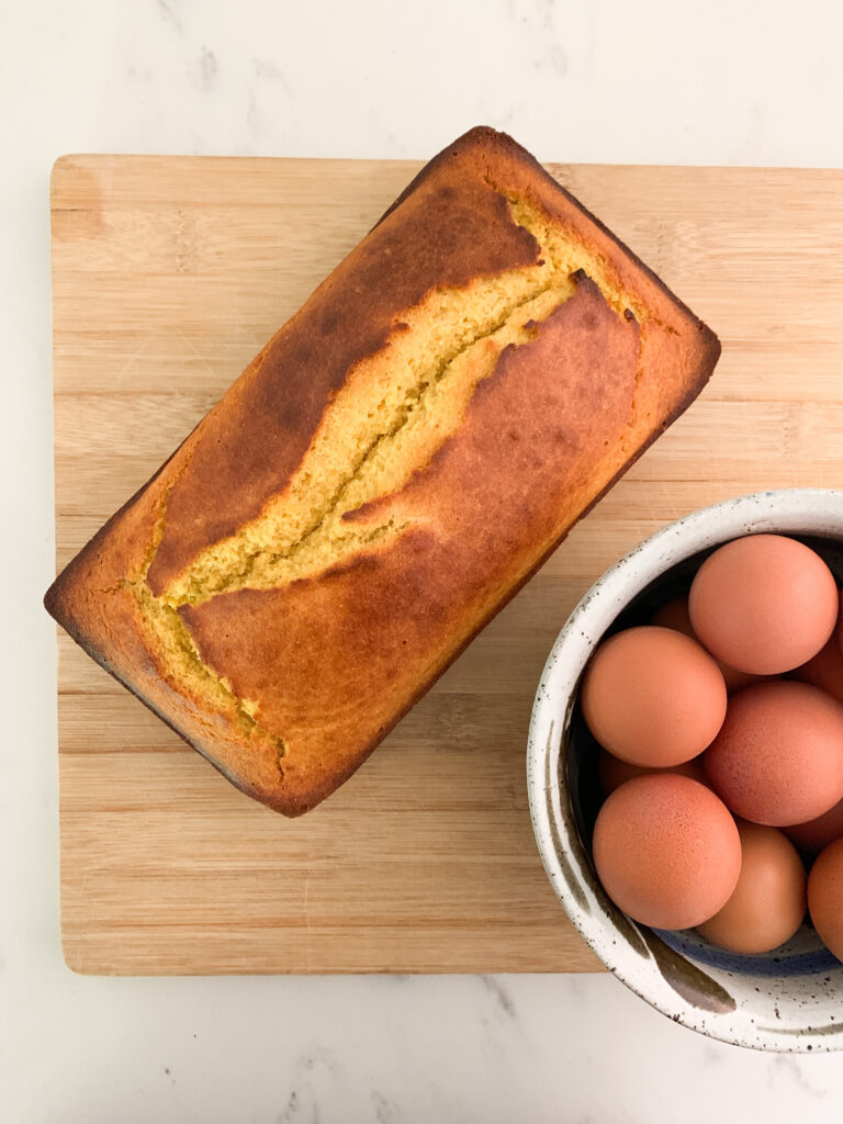 Fresh, unsliced cornbread and bowl of fresh un-cracked eggs on wood cutting board.