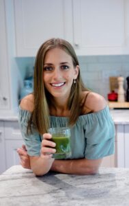 Becca in a teal top with a green smoothie in a kitchen