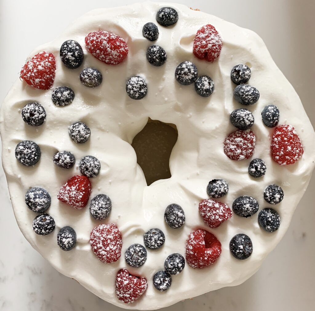 Birds-eye view of angel food cake with whipped cream, blueberries and raspberries.