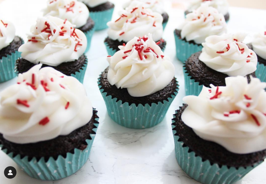 Chocolate cupcakes in blue wrapper with vanilla icing an white and red sprinkles on top