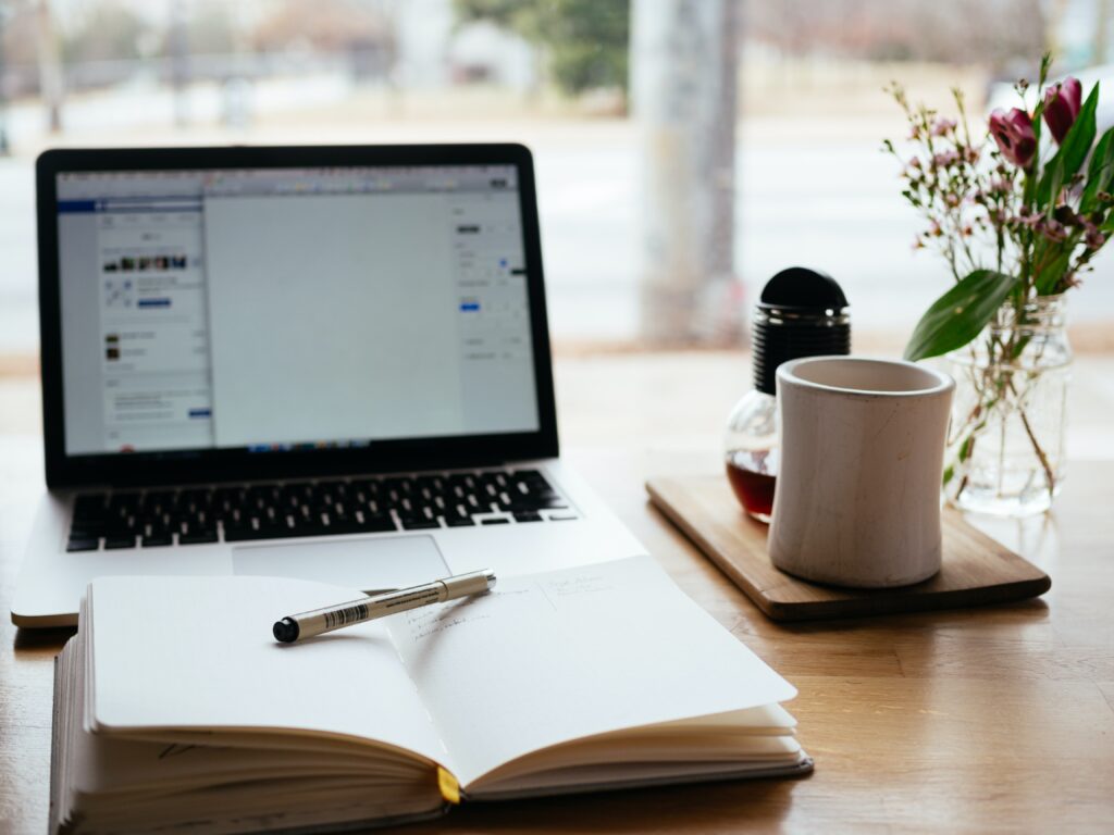 Laptop, notepad, pen, coffee mug and flowers on a wooden table