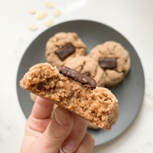 Almond butter cookie with chocolate with a bite taken out of it to show texture. Cookies on blue plate on counter behind.