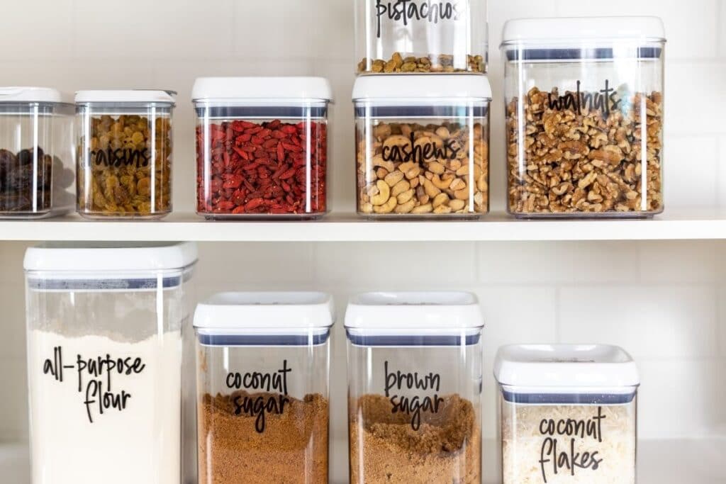 Pantry items in plastic containers on two shelves.