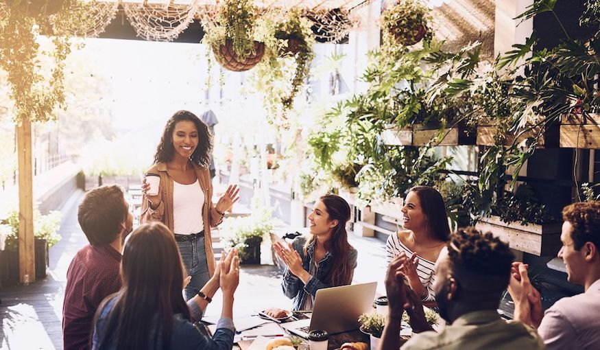 Female standing up at a table of people during a lunch meeting.