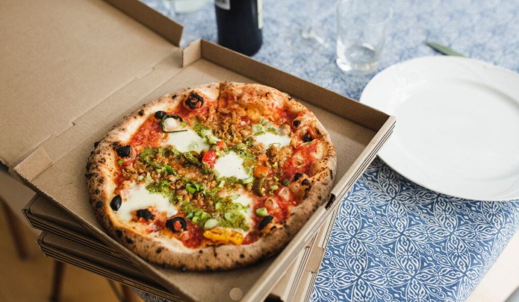 Pizza in open pizza box on top of two other pizza boxes next to empty white plate.