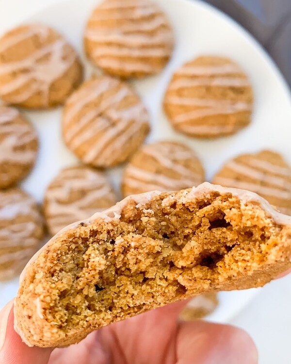 Almond flour pumpkin cookies on a plate and one cookie being held to camera with a bite taken out of it with a blue napkin in the right corner.