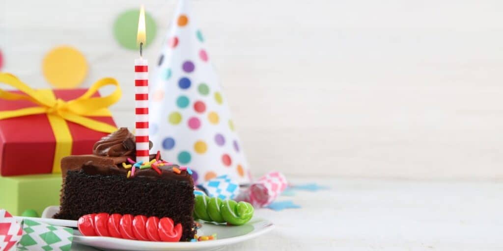 Birthday cake with candle, candies, hat and gift.