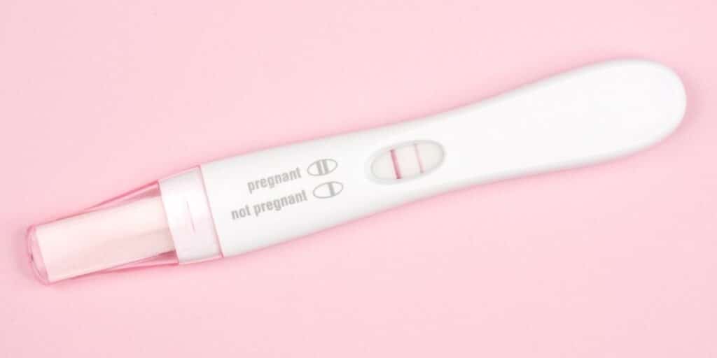 Positive pregnancy test on pink background.