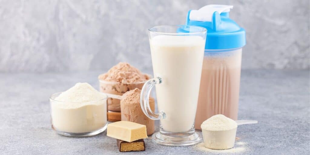 Protein powder, milk, protein bar, protein shake with grey backdrop.