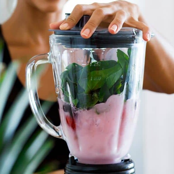 Protein shake ingredients in a blender with a hand on the lid.