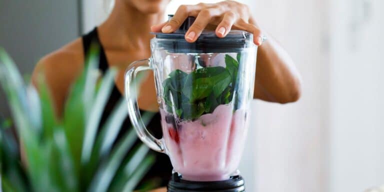 Protein shake ingredients in a blender with a hand on the lid.
