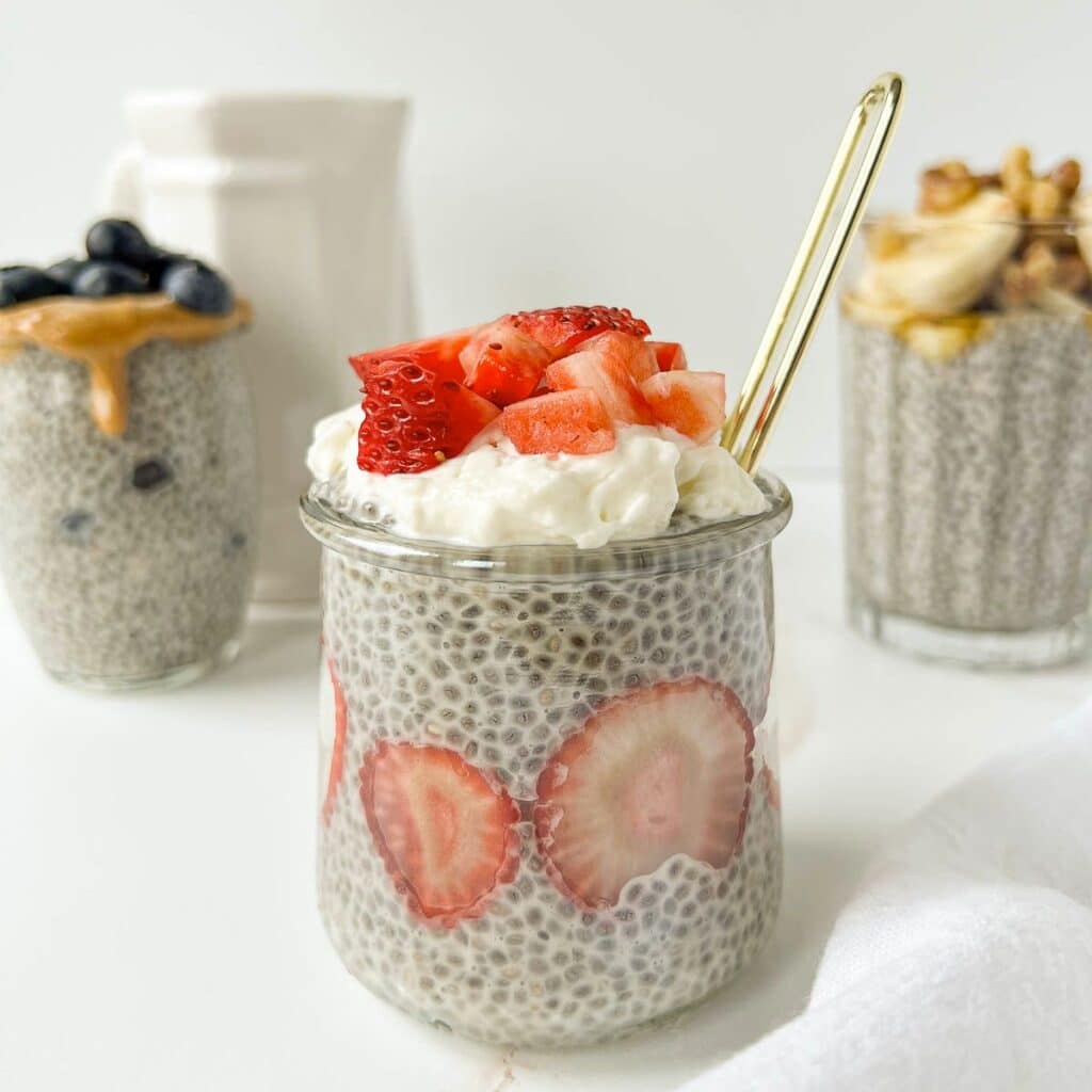 Three jars of chia pudding with different toppings. One in front with strawberries, two in back.