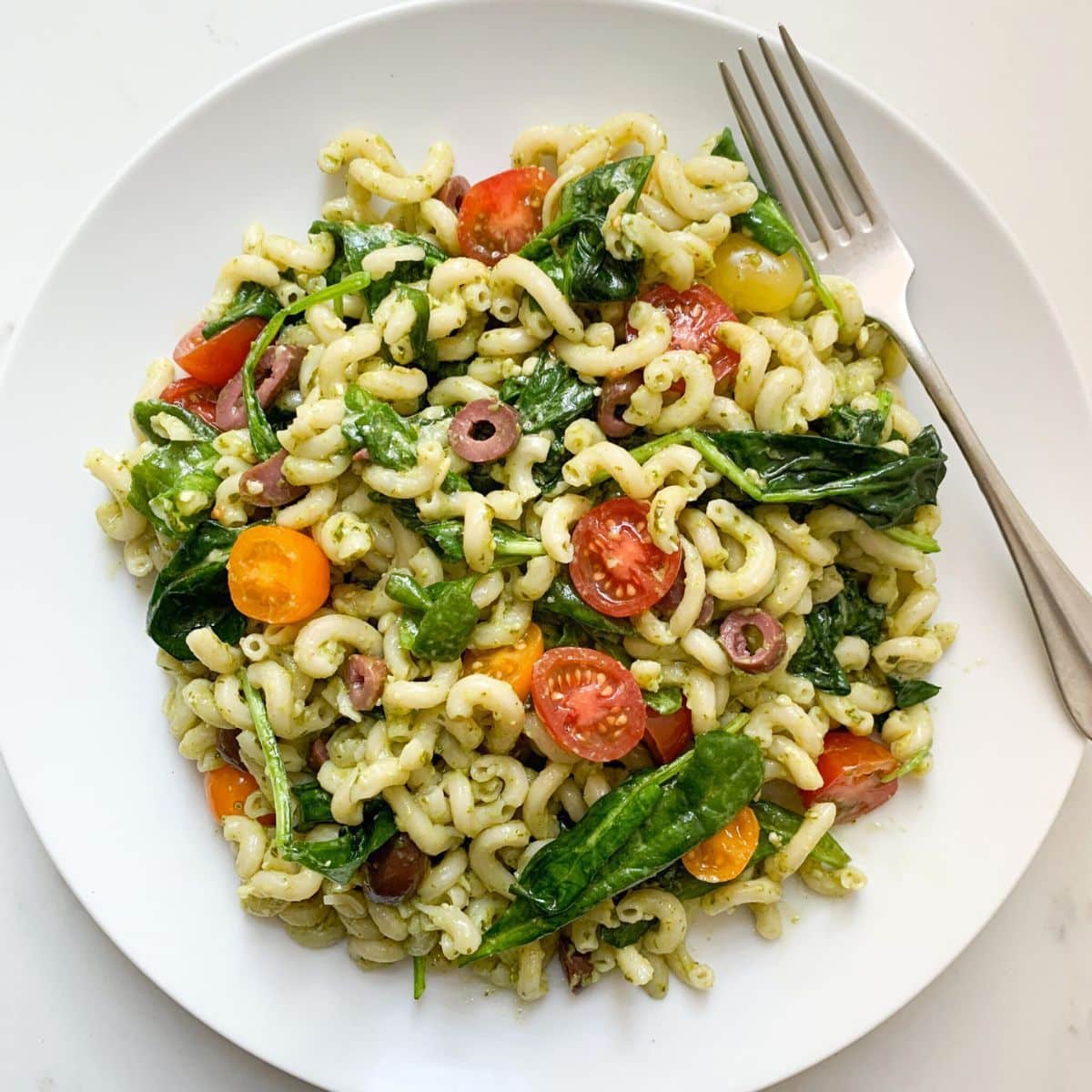 Pesto pasta salad on white plate with fork on top right.