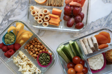 Three adult lunchables in glass containers on a marble countertop.