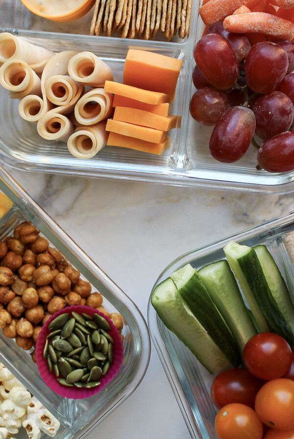 Three adult lunchables in glass containers on a marble countertop.