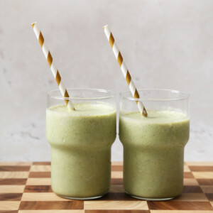 Two green smoothies with striped straws.