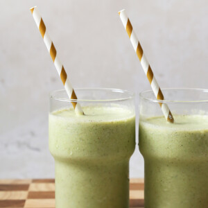 Close up of two green smoothies with striped straws.
