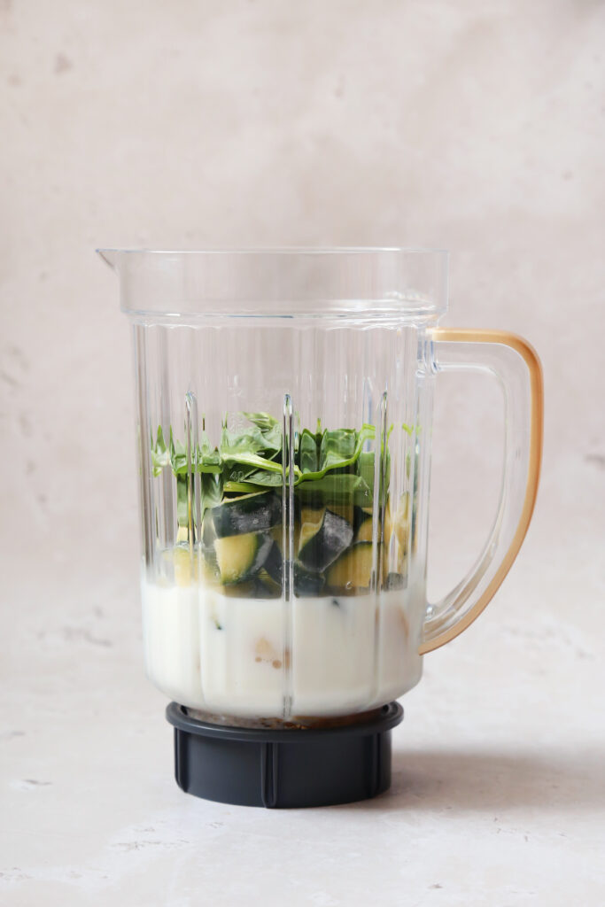 Zucchini smoothie ingredients in a blender on a countertop.