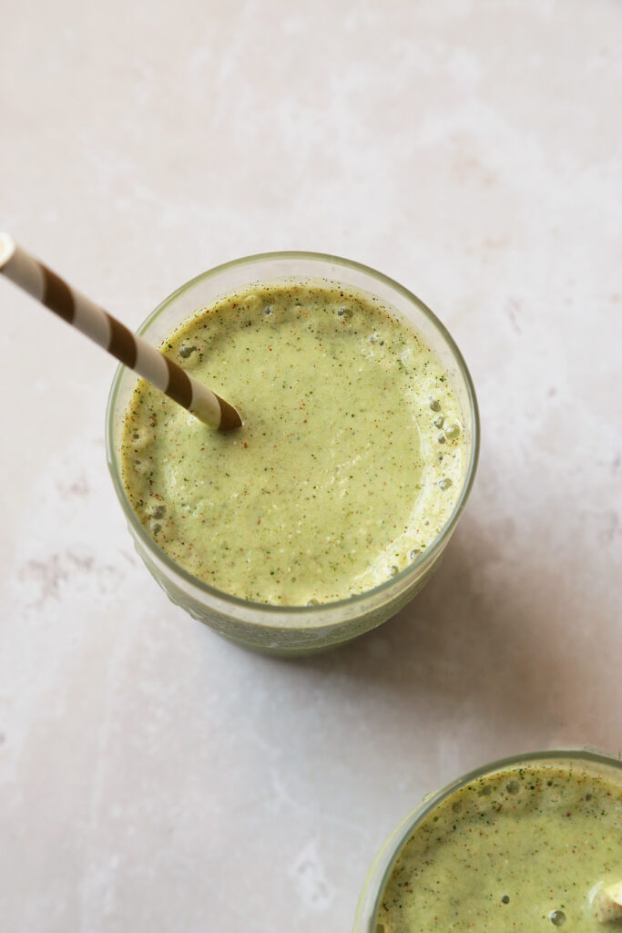 Overhead image of green smoothie with striped straw.