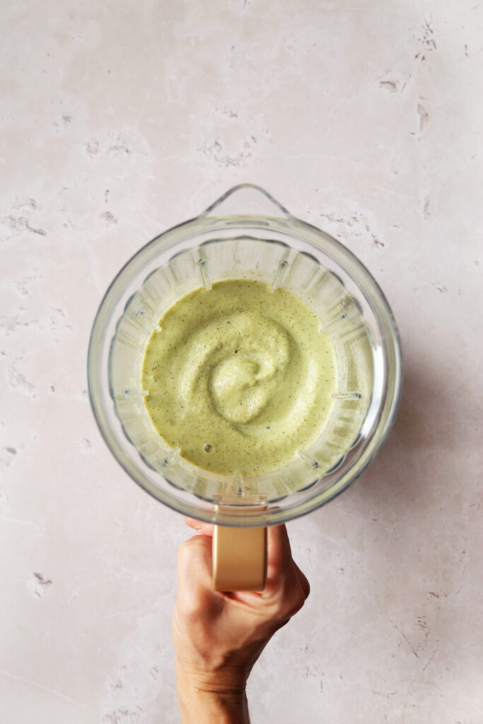Hand holding blender with green smoothie in it.