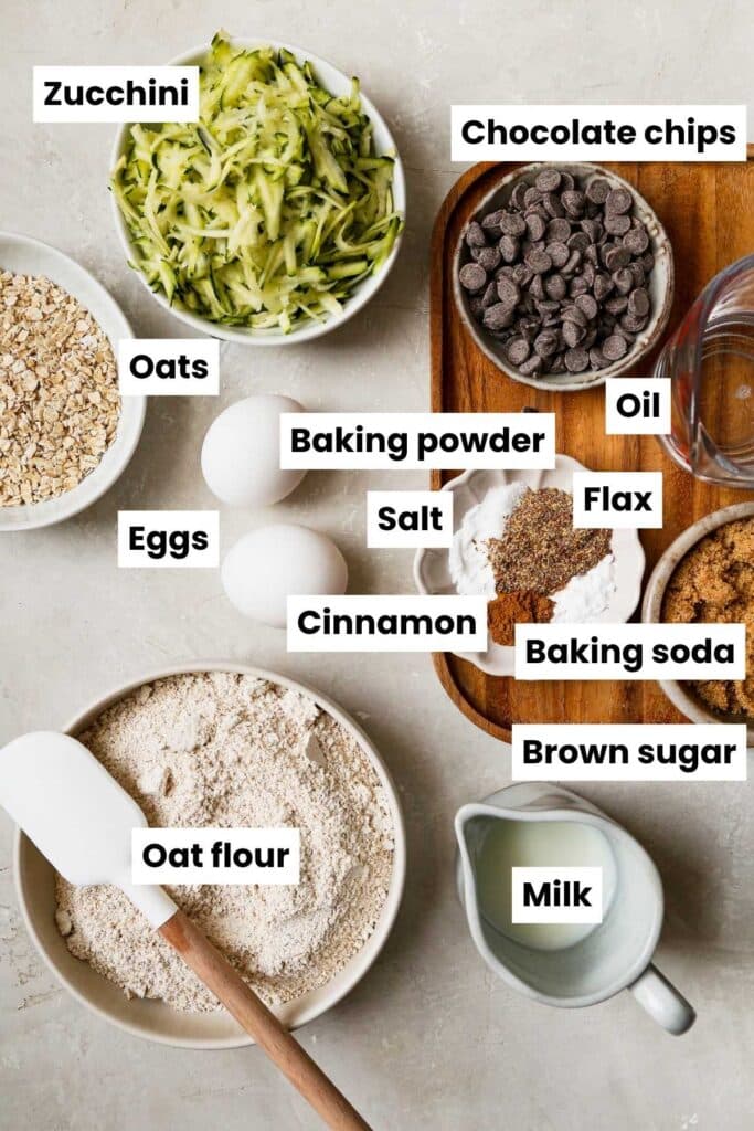 Overhead ingredient image that includes the following ingredients: shredded zucchini, oats, oat flour, chocolate chips, eggs, oil, flax, baking powder, baking sode, salt, cinnamon, brown sugar, and milk.
