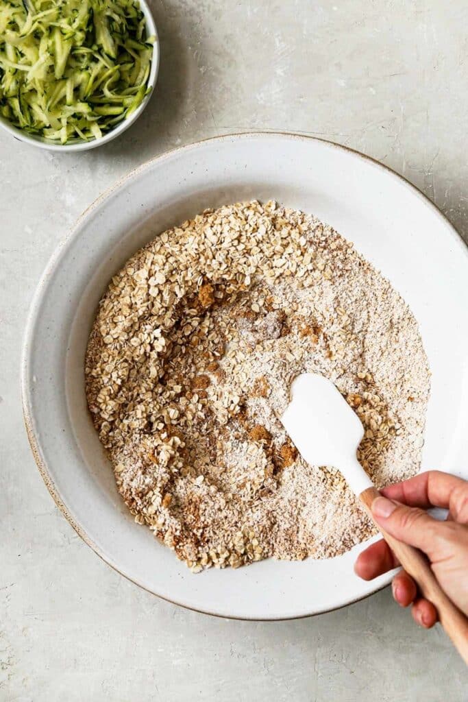 Overhead view of zucchini oatmeal bread dry ingredients being mixed in a white bowl.