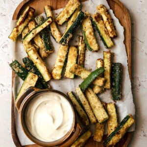 Overhead view of air fryer zucchini fries on wooden board with garlic aoili.