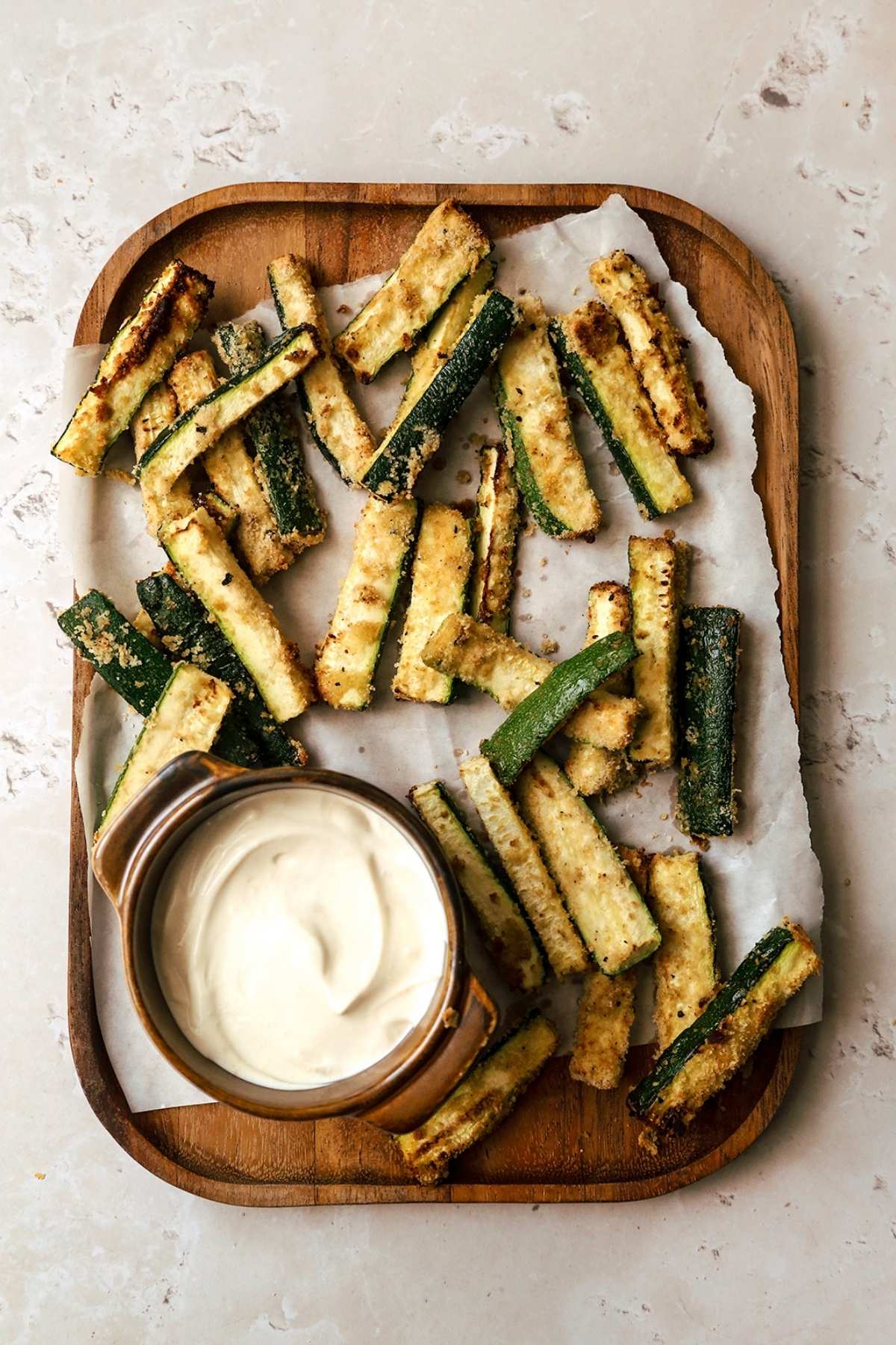 Overhead view of air fryer zucchini fries on wooden board with garlic aoili.