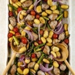 Sheet pan gnocchi with sausage and vegetables cooked on a pan with two wooden spoons.
