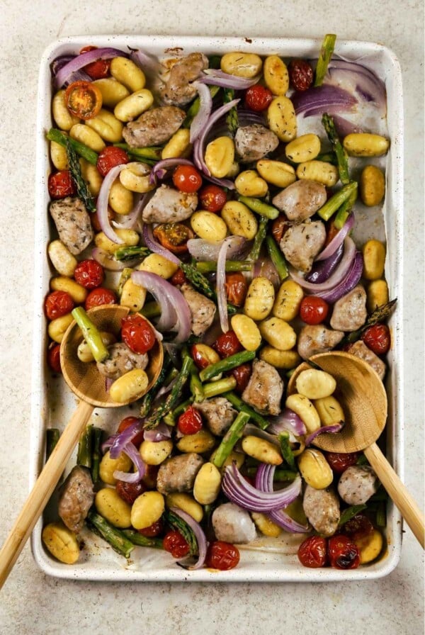 Sheet pan gnocchi with sausage and vegetables cooked on a pan with two wooden spoons.