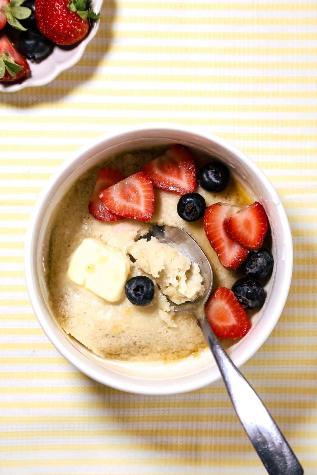 Pancake bowl with berries and melting butter on a yellow stripped background.