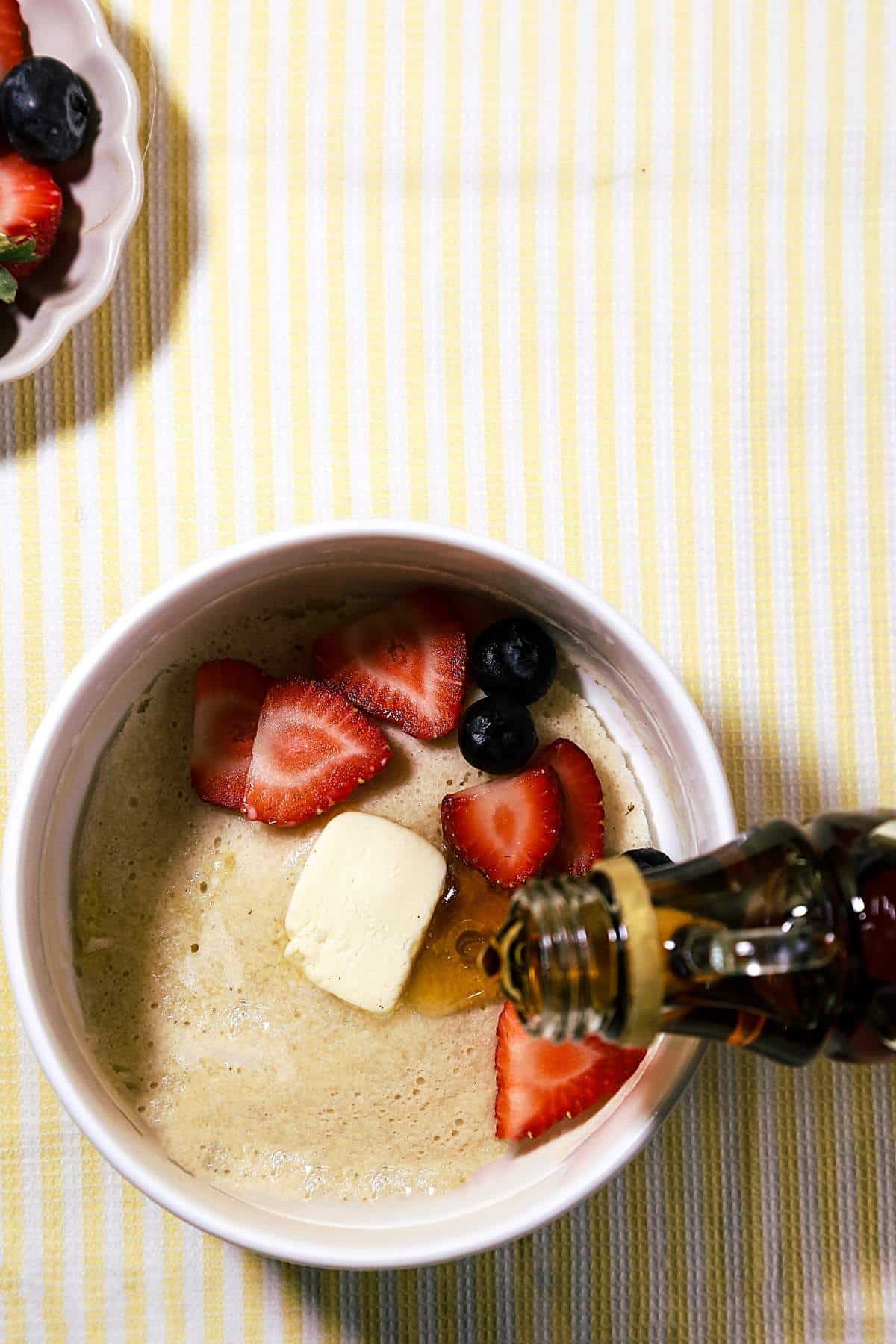 Microwave pancake with berries, butter, and maple syrup on a yellow stripped background.