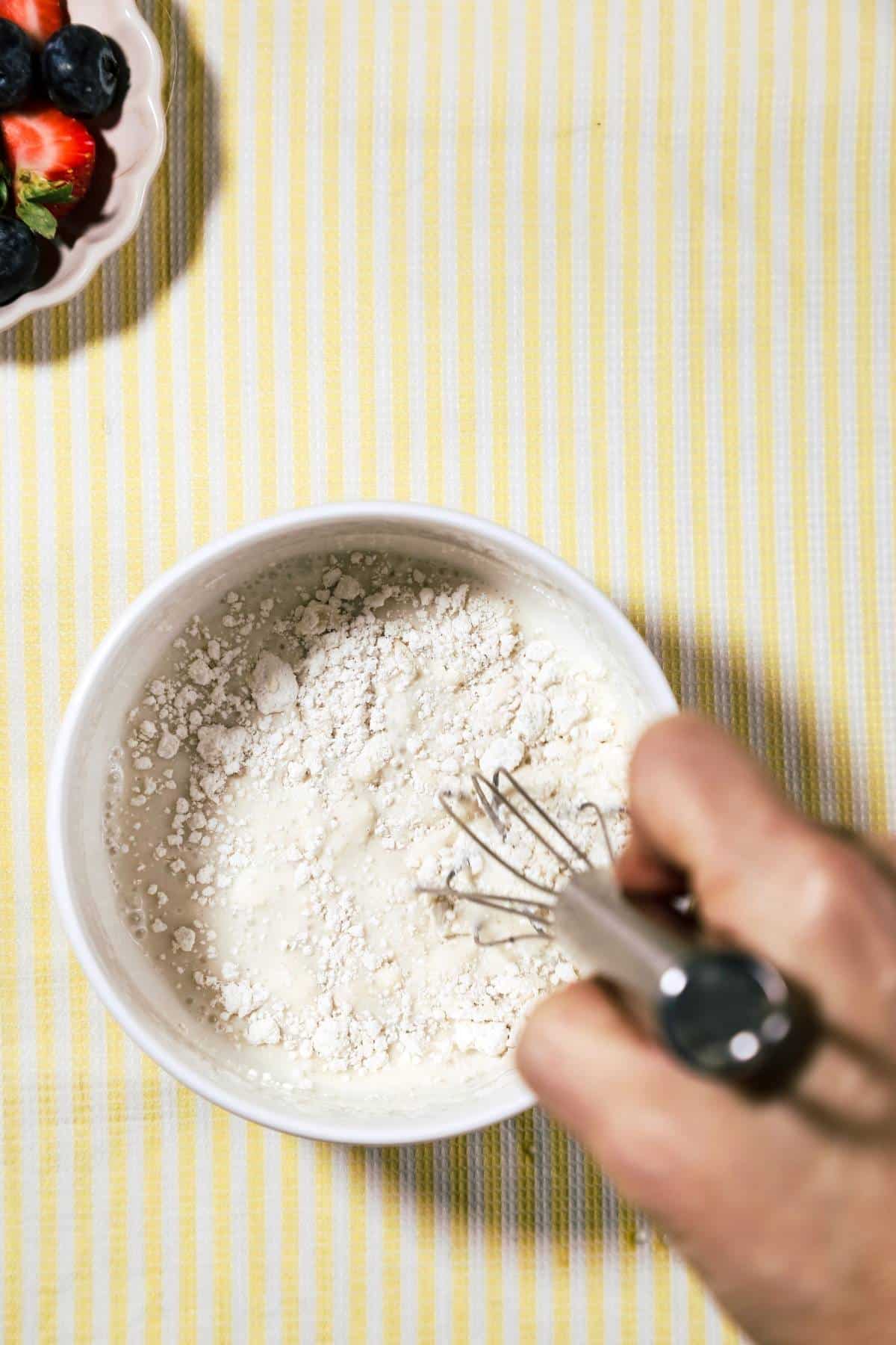 Bowl of pancake mix and milk being mixed on stripped yellow background.