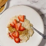 Rice cooker oatmeal in a white bowl with a spoon and strawberries on top.