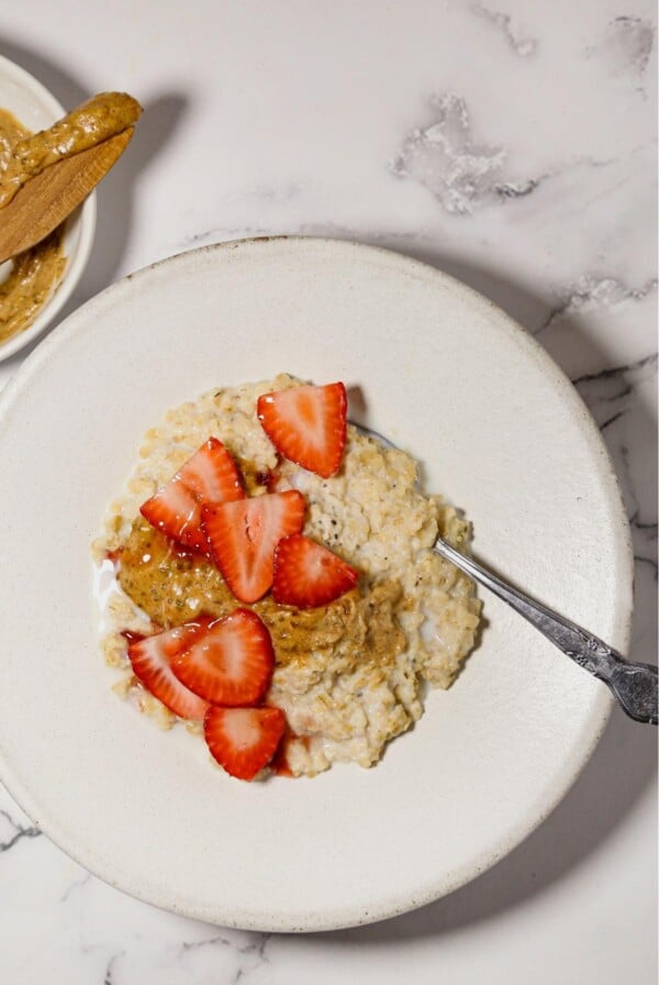 Rice cooker oatmeal in a white bowl with a spoon and strawberries on top.