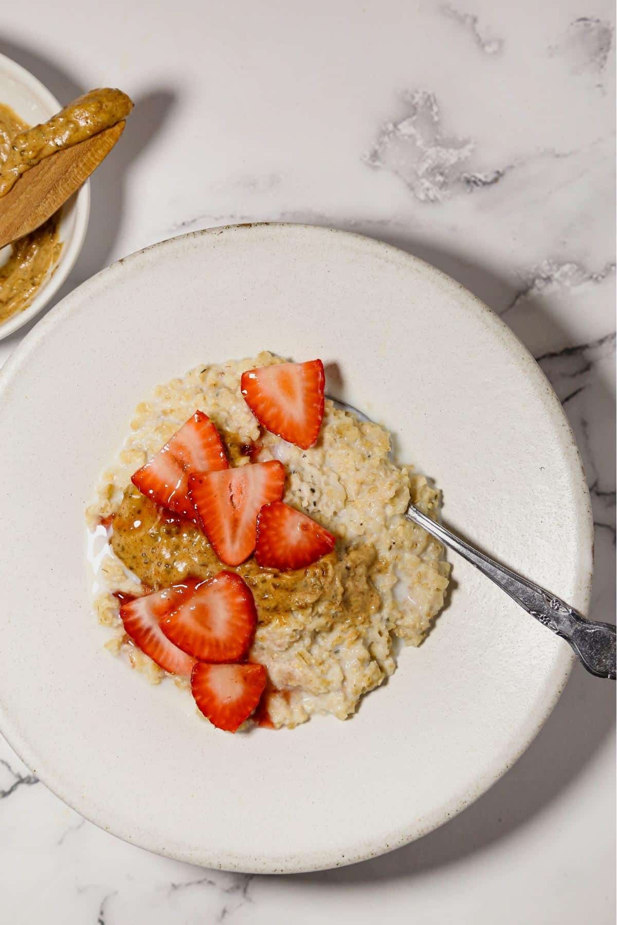 Rice cooker oatmeal in a white bowl with a spoon and strawberries on top.