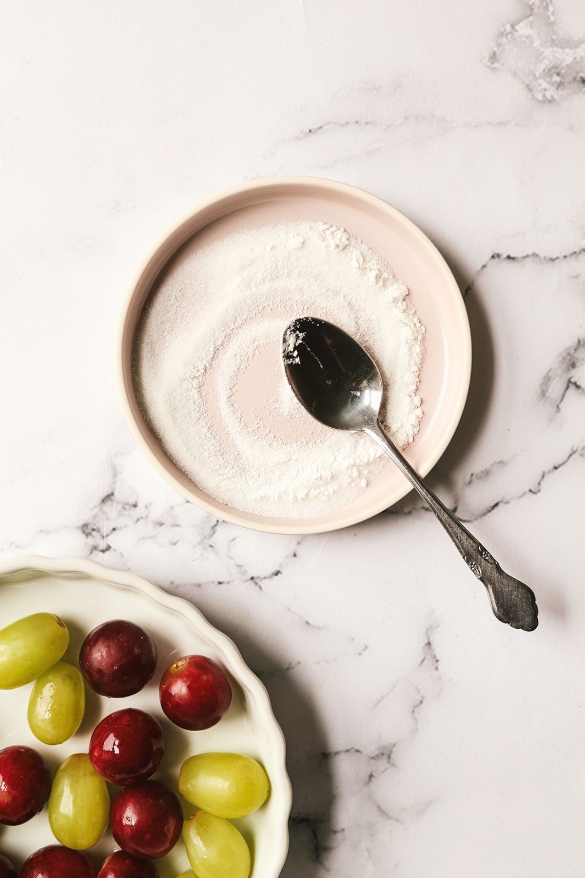 Two plates: one with grapes and one with sugar mixture.