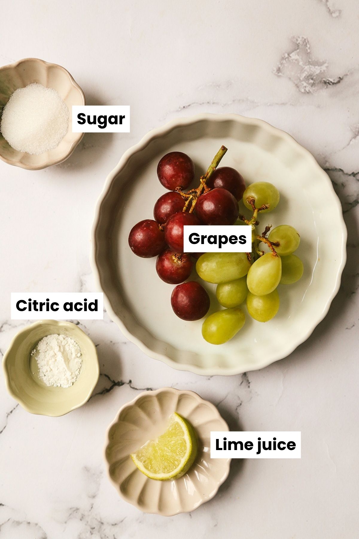 Overhead ingredients shot that includes red and green grapes, sugar, lime juice, and citric acid.