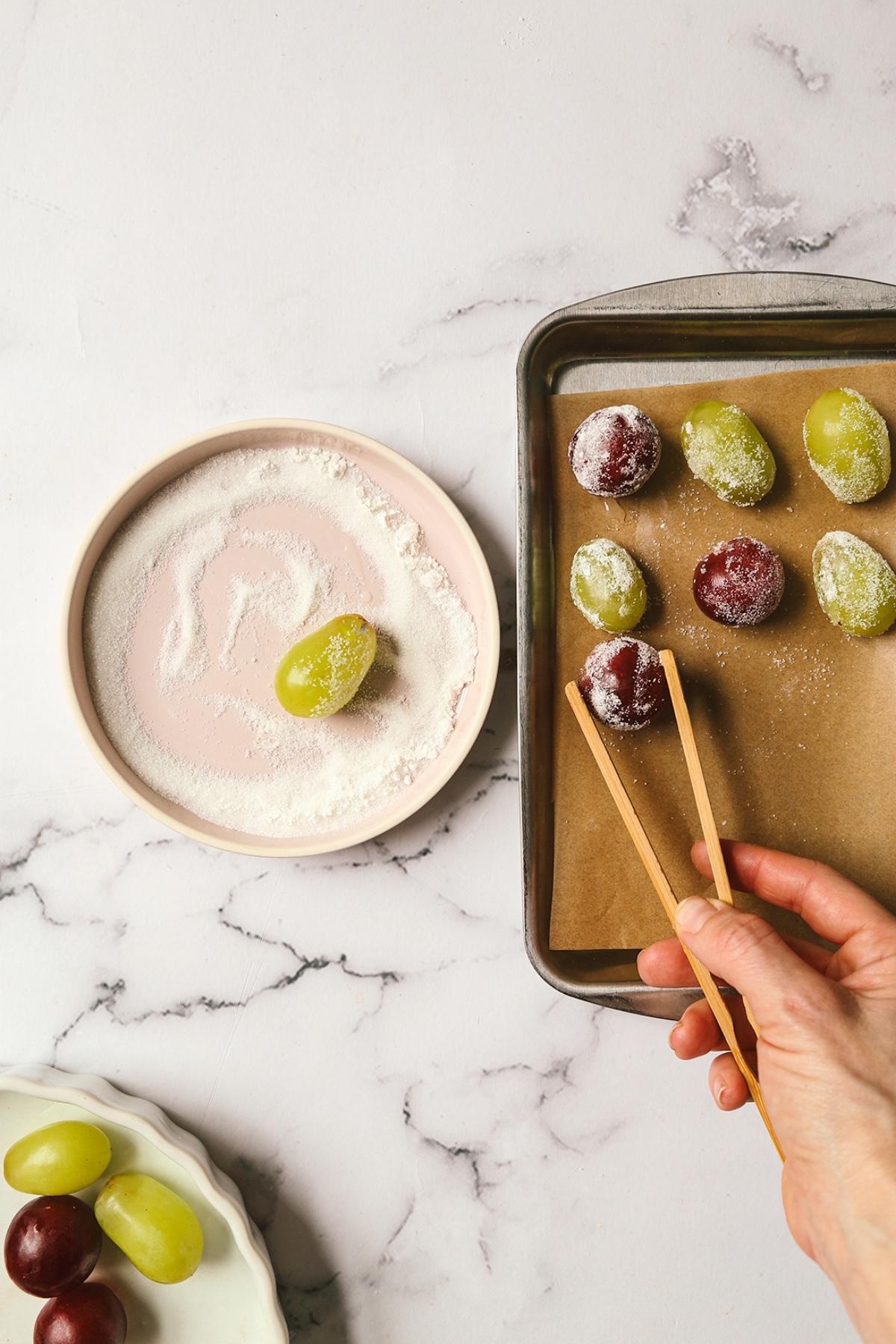 Grapes being placed on a cookie sheet from a sugar mixture on a plate.