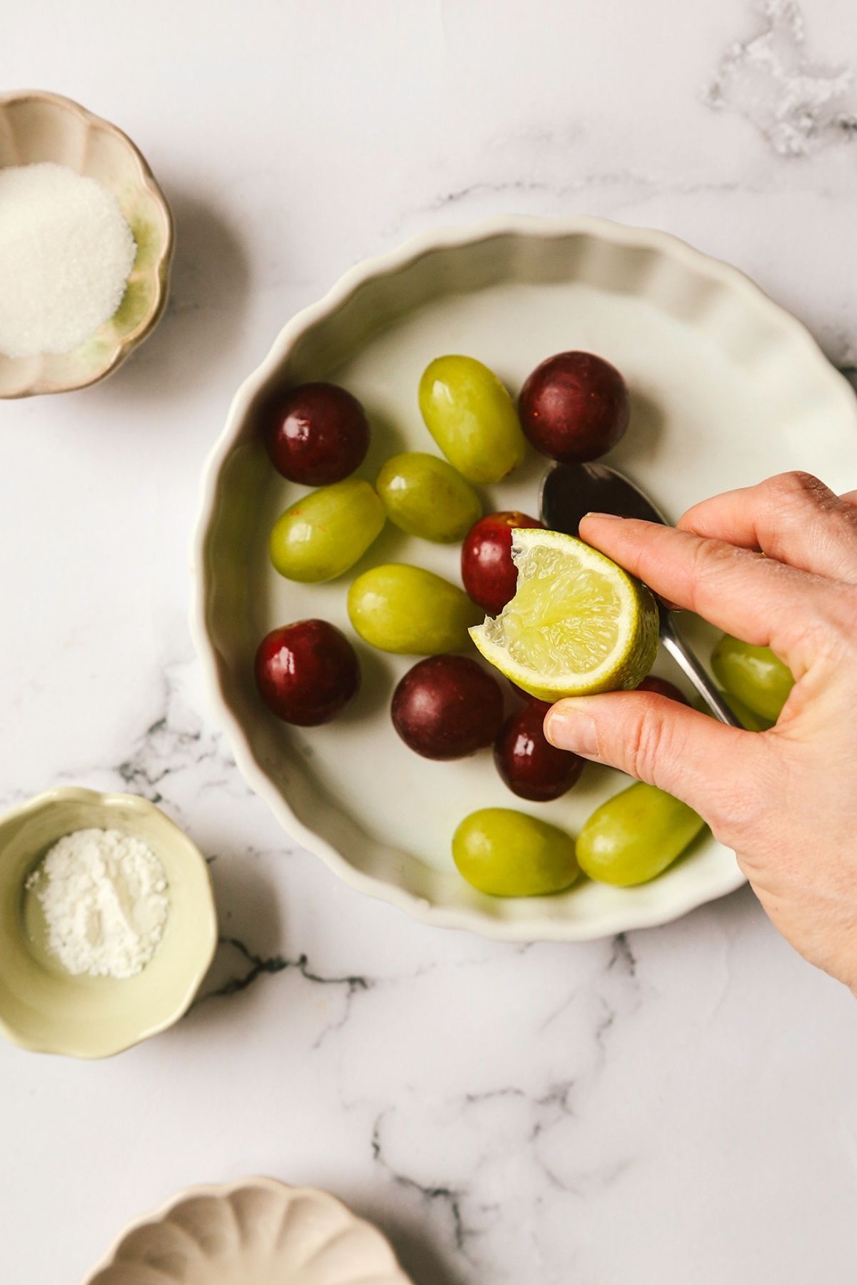 Green and red grapes on a plate with lemon being squirted onto them.