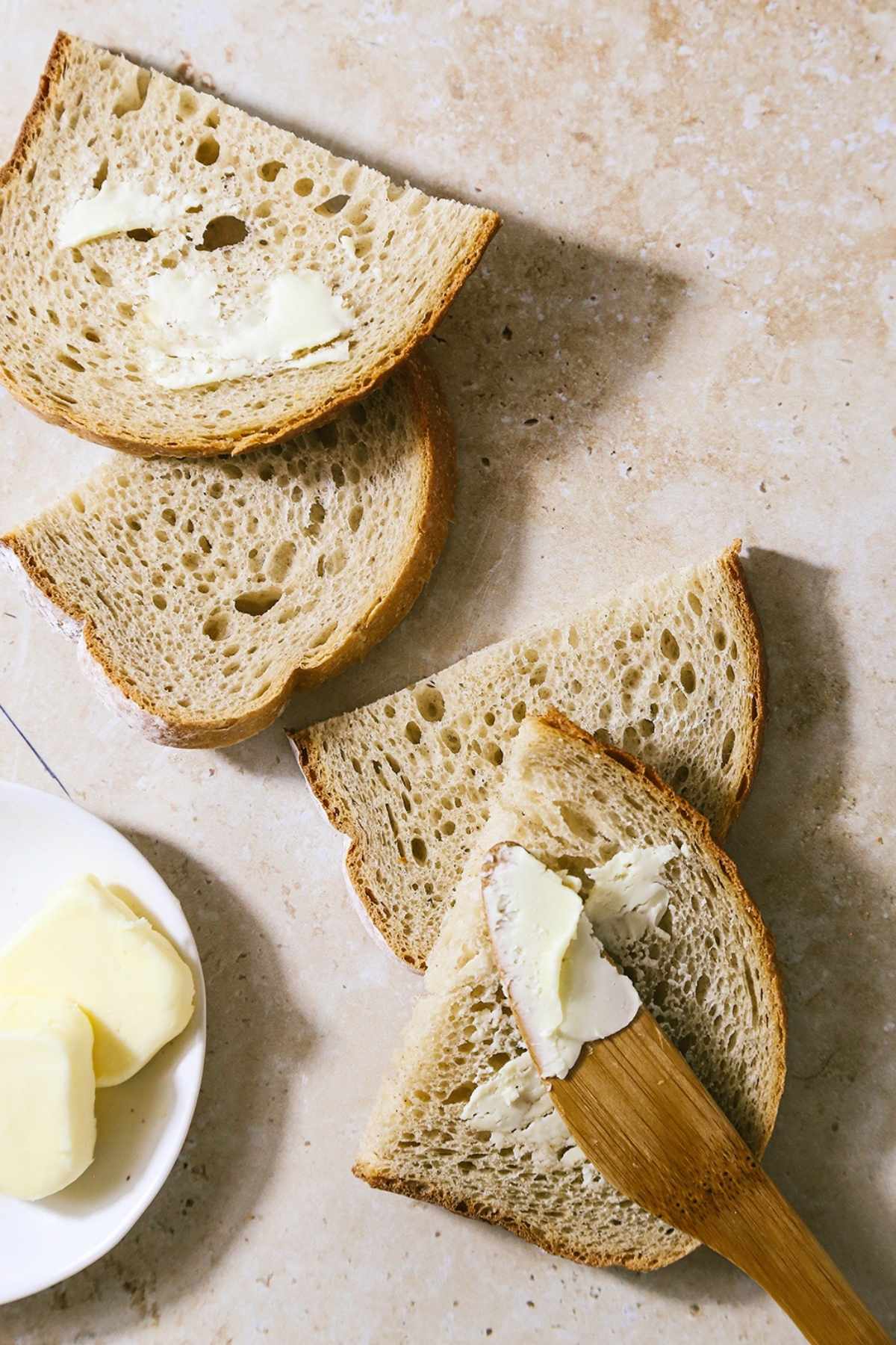 Overhead shot of four half sliced of sourdough with butter on them.